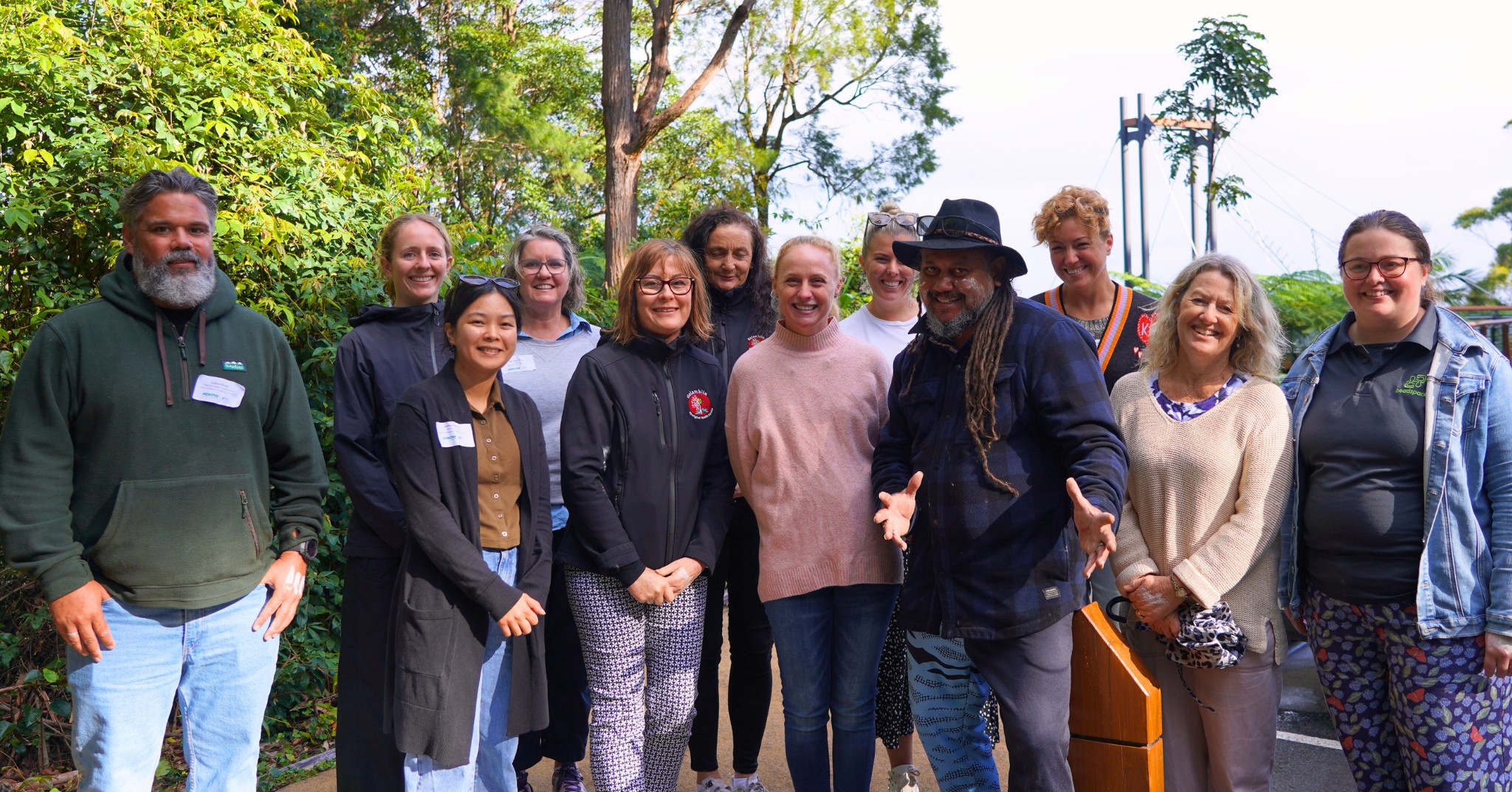Smiling group of Cultural Awareness Training participants and facilitators gathered on a path among trees, with a cultural facilitator welcoming with open arms
